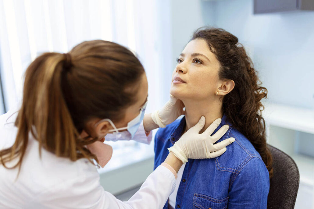 Doctor examines neck of female patient to look for signs of thyroid disease