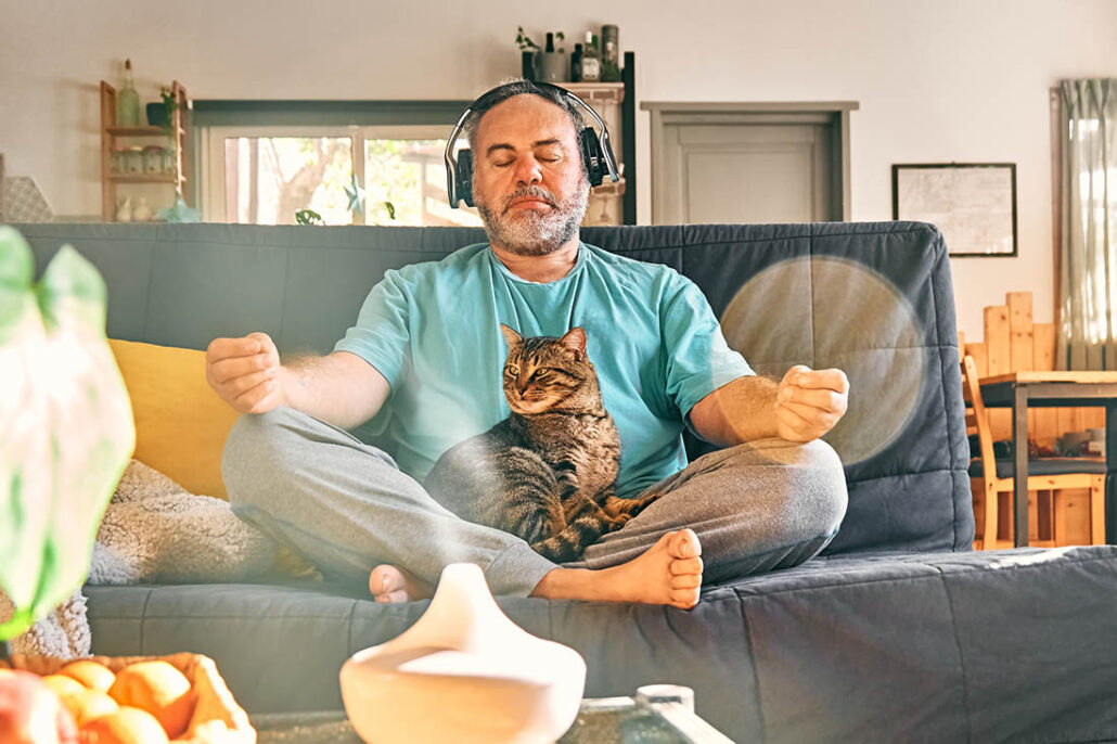 Middle-aged man meditates on his couch with his cat for stress reduction