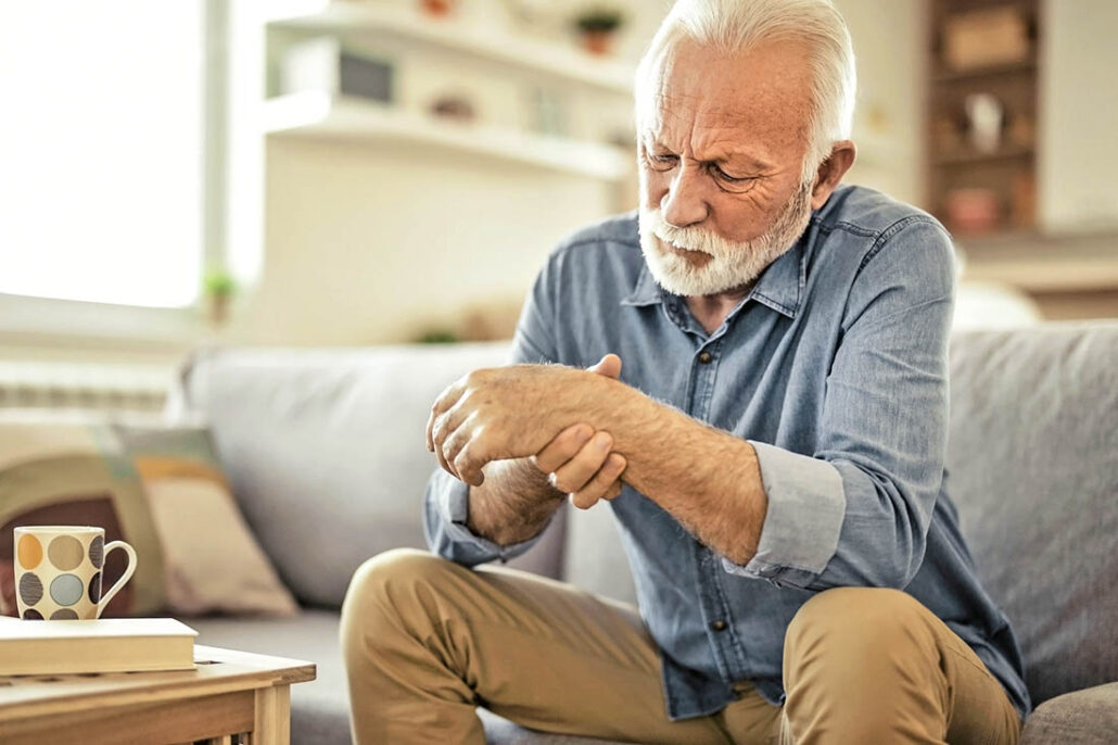 Elderly man holding his wrist, experiencing joint pain from rheumatoid arthritis