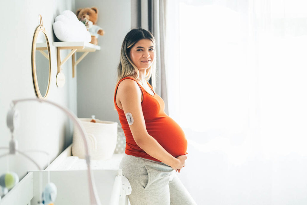 A very pregnant young woman with gestational diabetes wearing a CGM