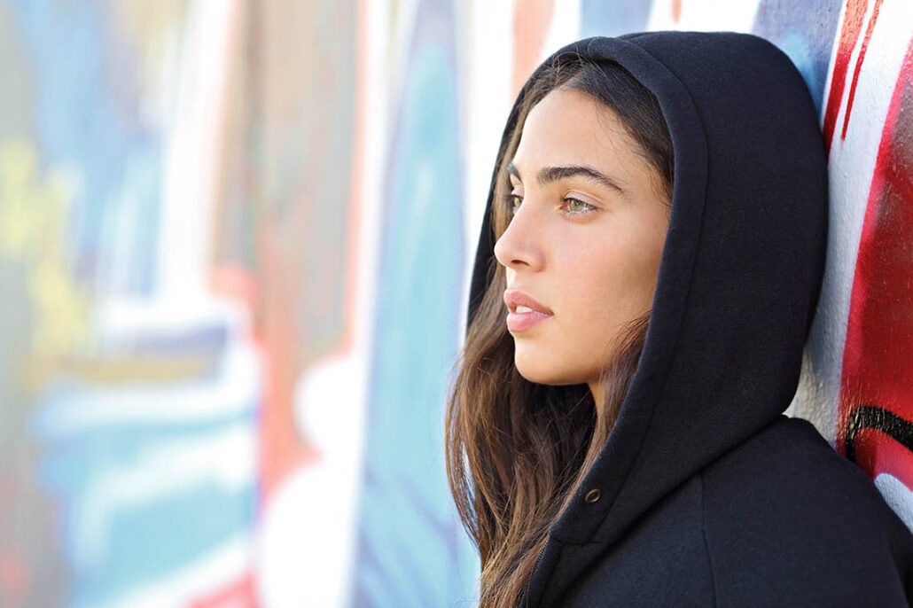 A sad young woman leaning against a wall looking deep in thought