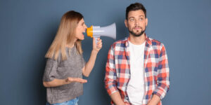 frustrated young woman yells into a megaphone while her boyfriend looks unfazed
