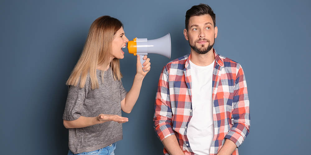 frustrated young woman yells into a megaphone while her boyfriend looks unfazed