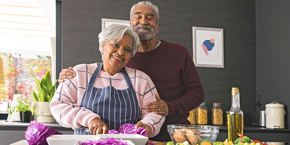 A slightly overweight attractive middle-aged biracial couple cook in the kitchen together
