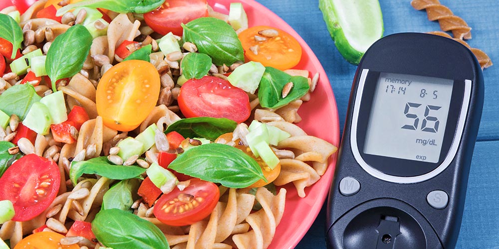glucose meter with a low blood sugar reading of 56 mg/dL next to a plate of pasta