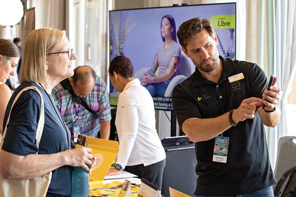 A vendor behind a table shows a customer something on his cell phone