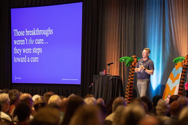 A male speaker stands on stage next to a big screen with a slide about curing diabetes
