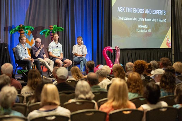Four speakers sit on stage giving a talk in front of a large audience