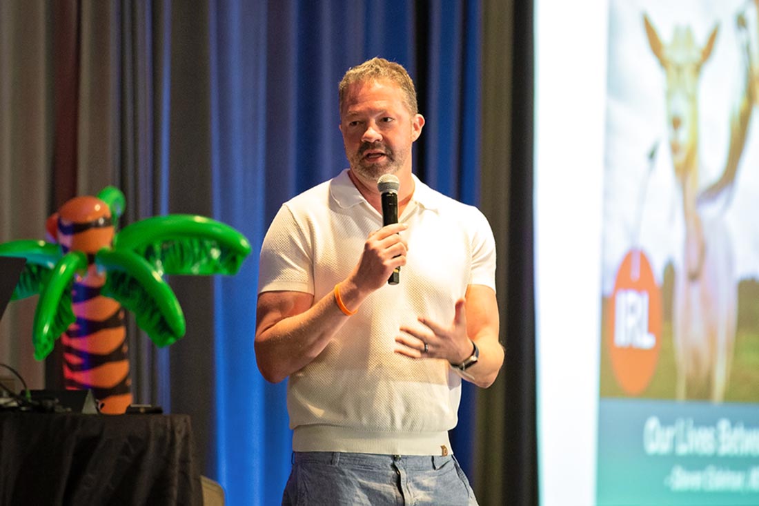 An educator stands on stage with a microphone giving a talk