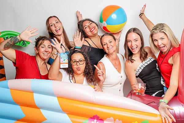 A group of women smile and wave as they pose with blown up beach toys