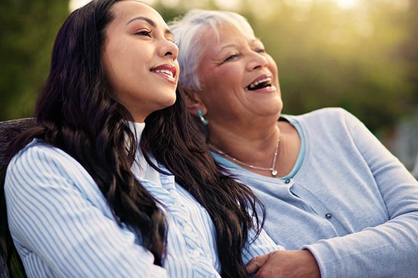 A mother and daughter sit on a bench and look out into the distance, laughing