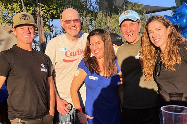 A group of five adults, one with a continuous glucose monitor on her arm, standing in the sun smiling at the camera